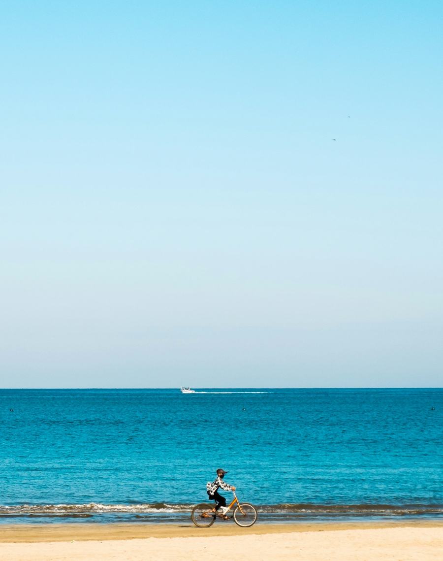 Ciclista pedalando pela areia à beira de um mar azul