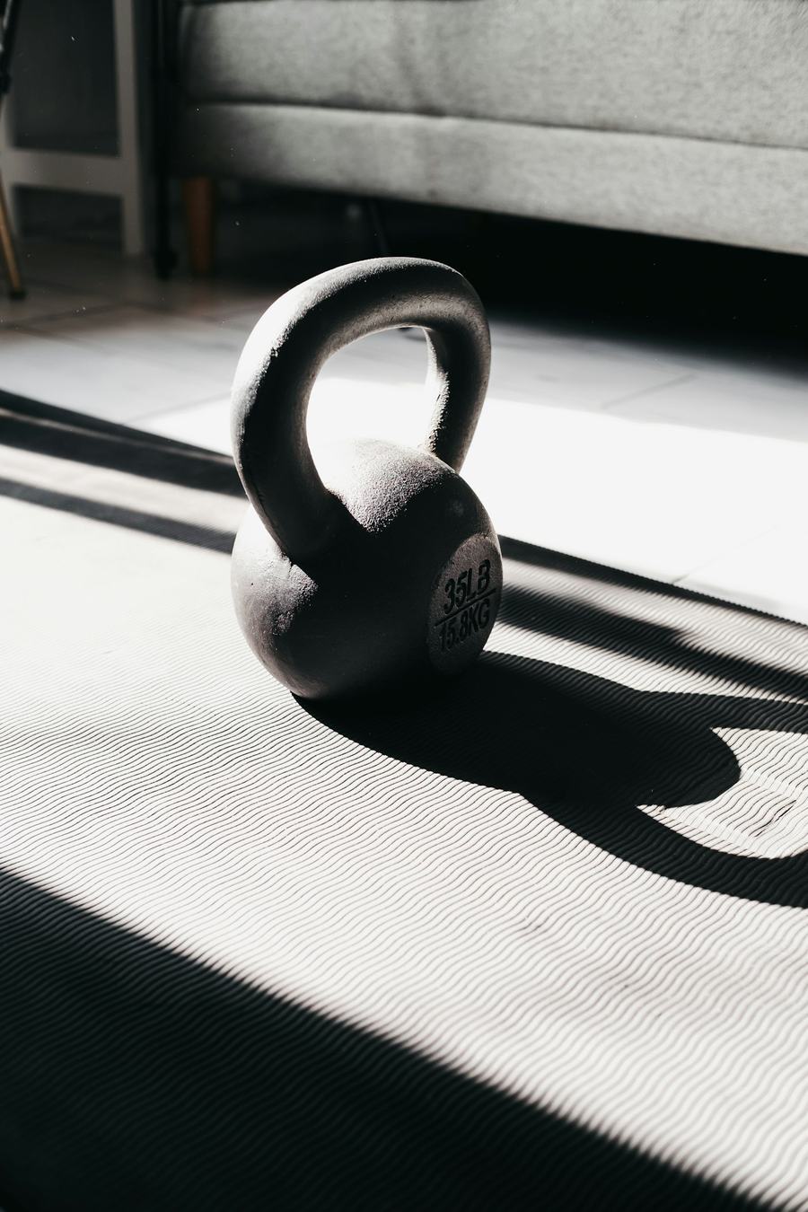 Kettlebell preto sobre tapete de treino iluminado pelo sol